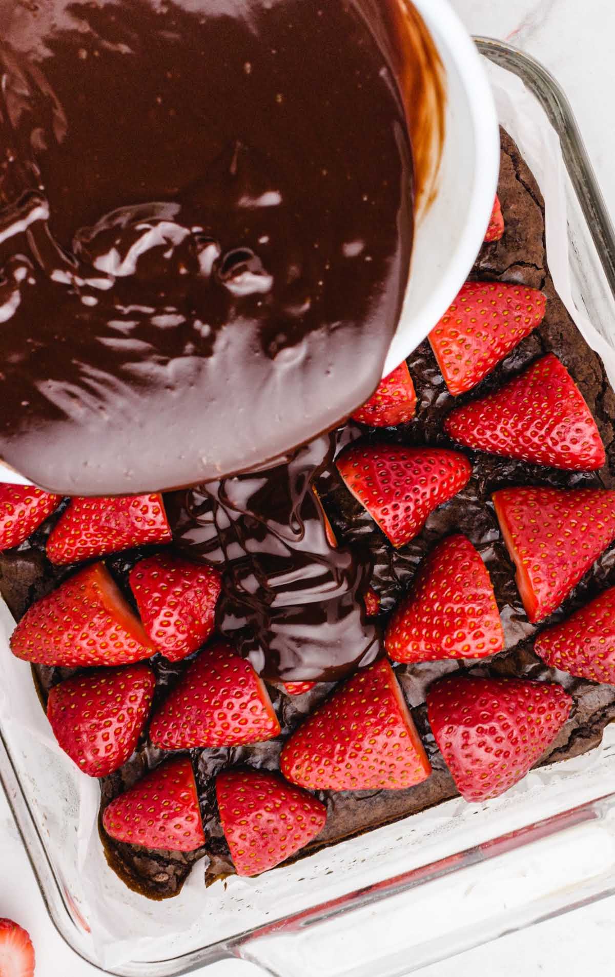 chocolate ganache being poured over the strawberries in a baking dish