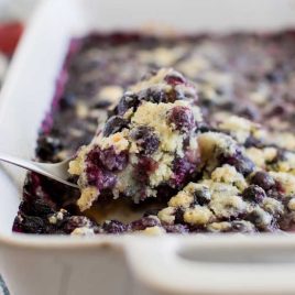 close up shot of blueberry cobbler in a baking dish with a spoonful of cobbler