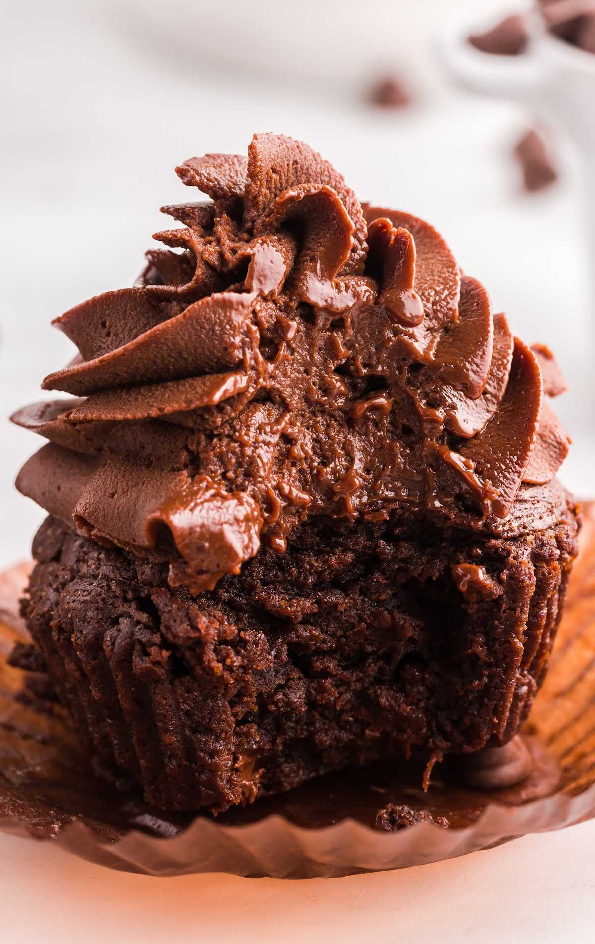 close up shot of a brownie cupcake topped with a chocolate ganache with a bite taken out of it