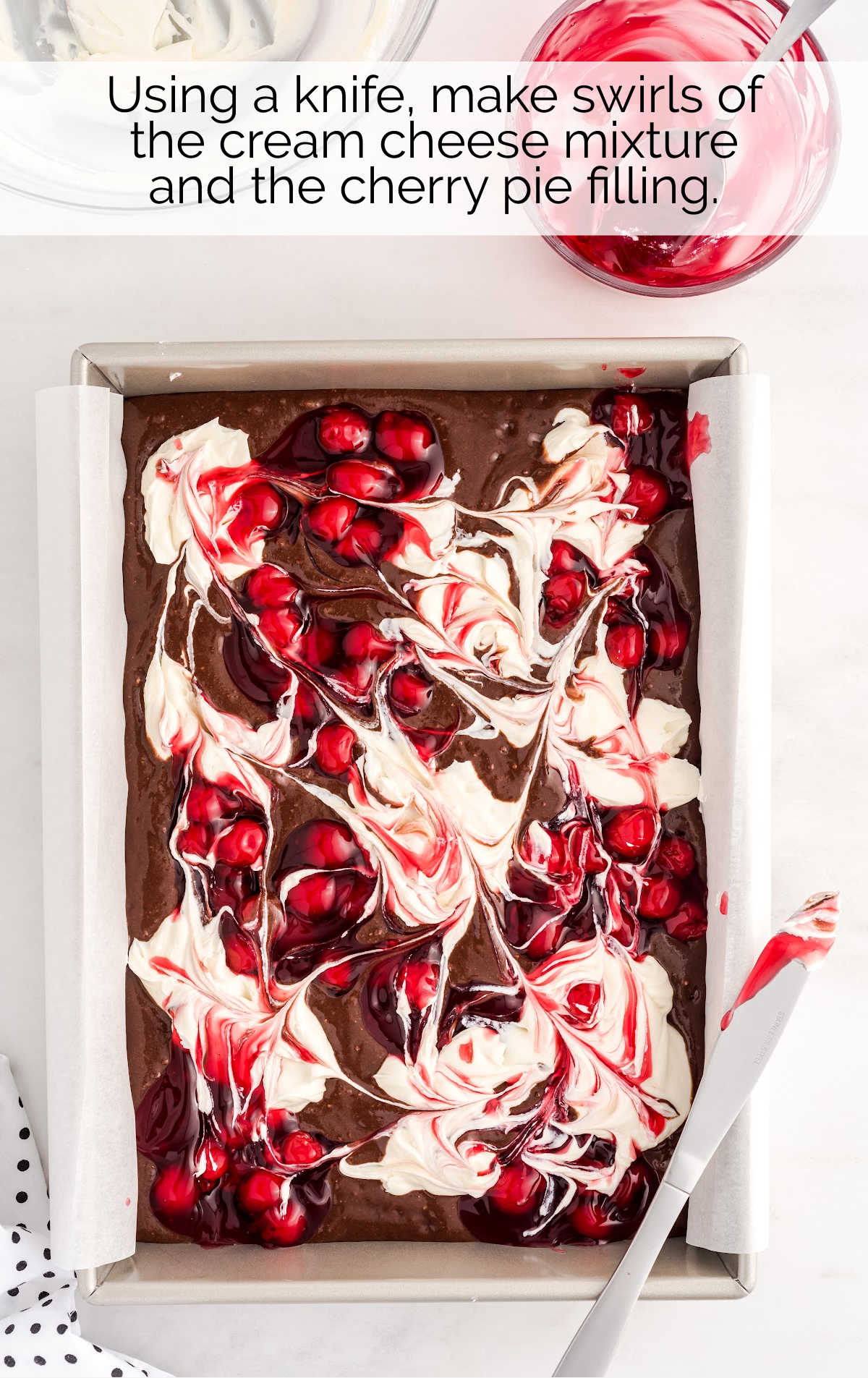 cream cheese mixture and cherry pie filling swirled on top of the brownie batter in a baking pan