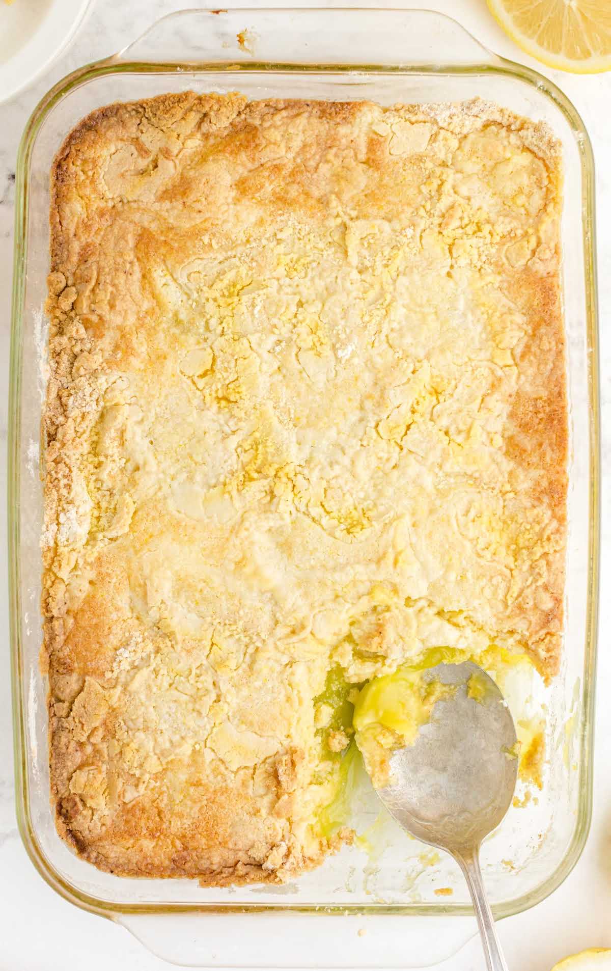 overhead shot of a baking dish of lemon cake with a piece taken out of it with a spoon