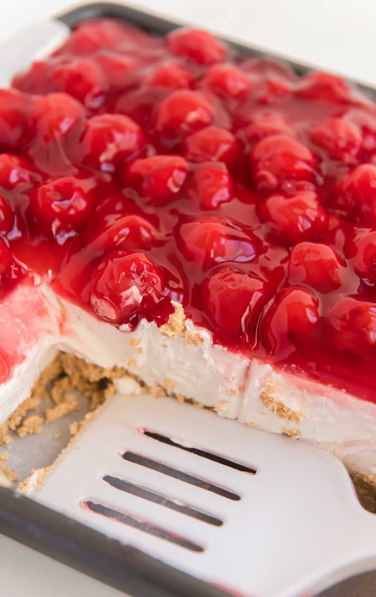cheesecake topped with cherry pie filling in a baking dish with a spatula