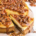 close up shot of a cheesecake topped with pecans and caramel glaze with a slice being removed
