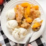 close up over head shot of a slice of Peach Cobbler with ice cream on a plate with a spoon