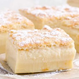 slices of Magic Custard Cake on a wooden board with a spatula picking one up