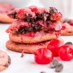 a close up shot of Cherry Chocolate Chip Cookies stacked on top of each other with cherries on the side