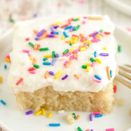 close up shot of a slice of Vanilla Crazy Cake on a plate topped with sprinkles and frosting