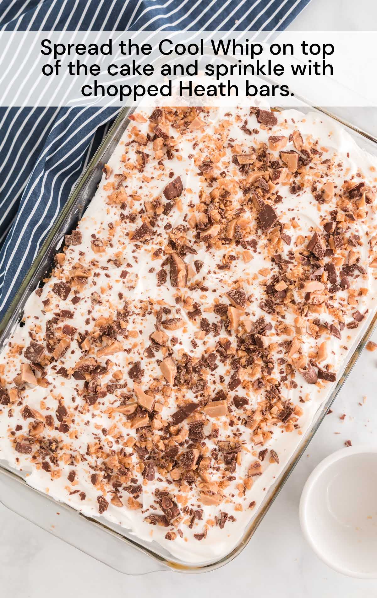 cool whip spread on top of the cake sprinkled with chopped heath bars in a baking dish